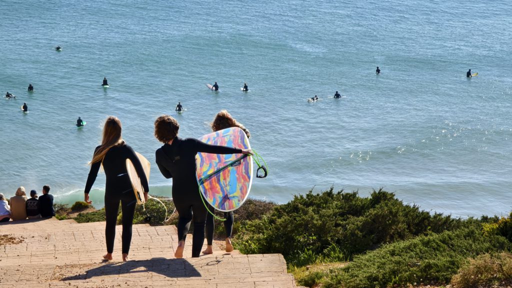 Three surfers with colorful boards walking toward the ocean on the Alentejo coast in Portugal