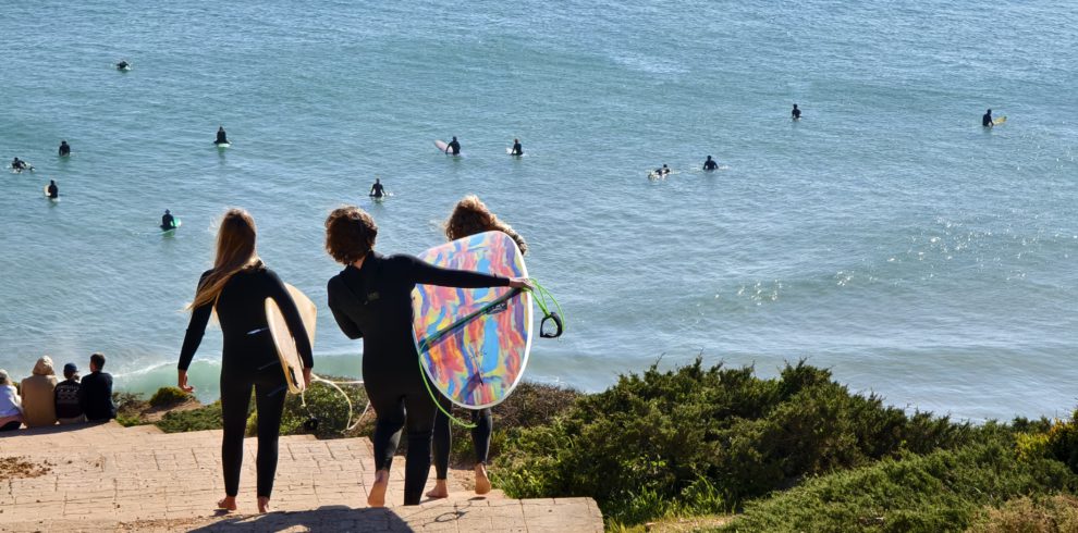 Three surfers with colorful boards walking toward the ocean on the Alentejo coast in Portugal